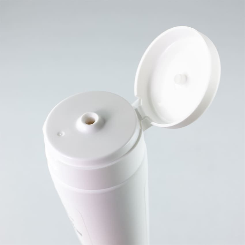 Dettaglio ravvicinato del tappo flip-top aperto di un tubo cosmetico bianco, che mostra l’apertura del dosatore. L'immagine enfatizza la praticità e l'igiene dell'erogazione del prodotto