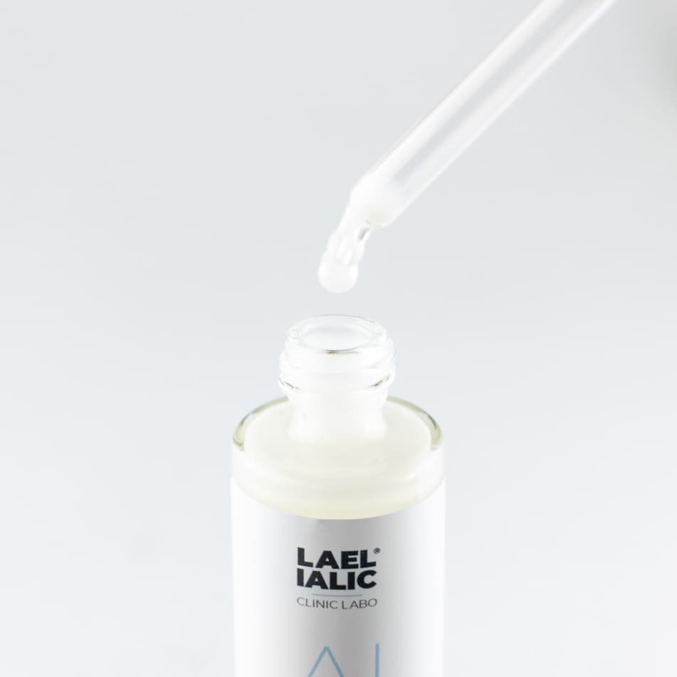 Dettaglio di un contagocce che rilascia il siero viso Pure Light Skin Plus di Lael Ialic in un flacone bianco, su sfondo chiaro. Trattamento idratante con acido ialuronico per una pelle luminosa e protetta.