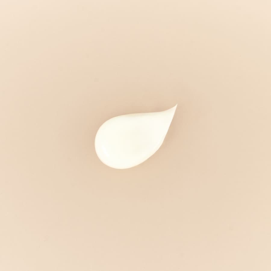 Immagine di una goccia di crema bianca su uno sfondo neutro, rappresentante la texture delicata e fluida del prodotto.