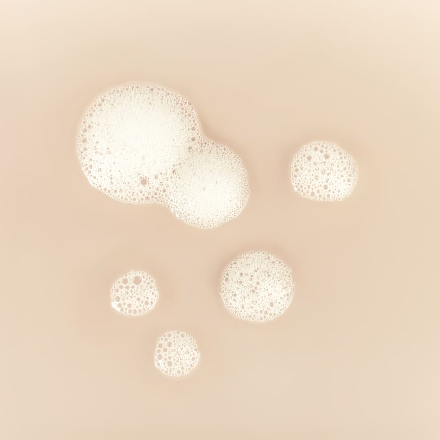 Immagine di bolle di schiuma su fondo beige, probabilmente riferite a un prodotto cosmetico come il detergente viso.